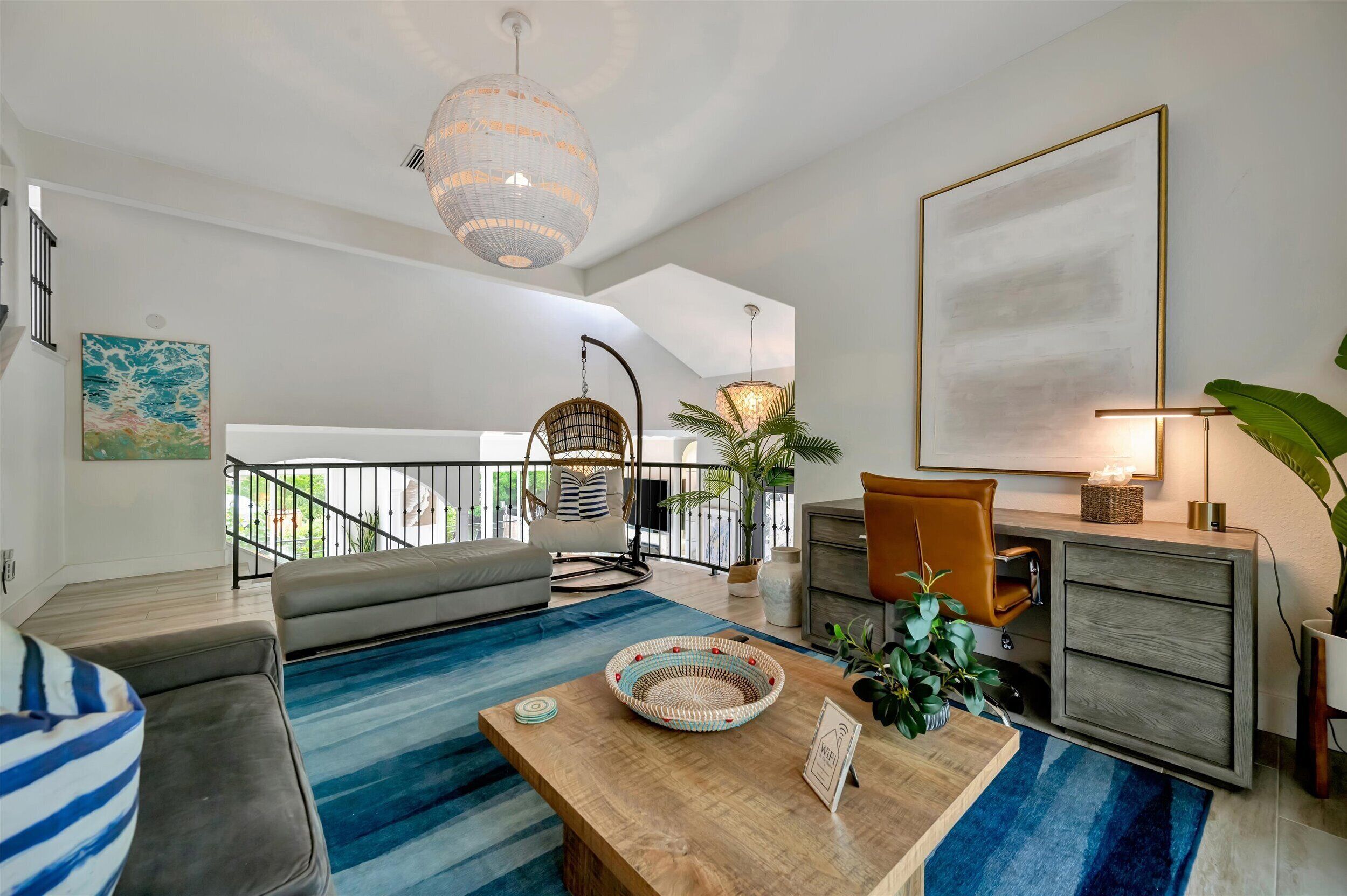 Un salon moderne avec un canapé, une table basse en bois, un luminaire suspendu, un fauteuil et un grand tableau accroché au mur.