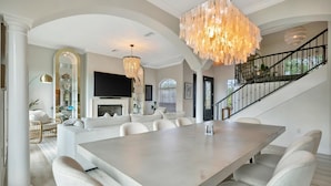 Une salle à manger spacieuse, dotée d’une grande table et de chaises, d’un lustre et d’un escalier menant à un niveau supérieur.