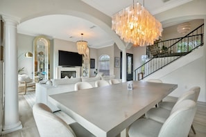 A spacious dining area with a large table and chairs, a chandelier, and a staircase leading to an upper level. - Modern Boho Home Avenida Del Mare (Siesta Key)