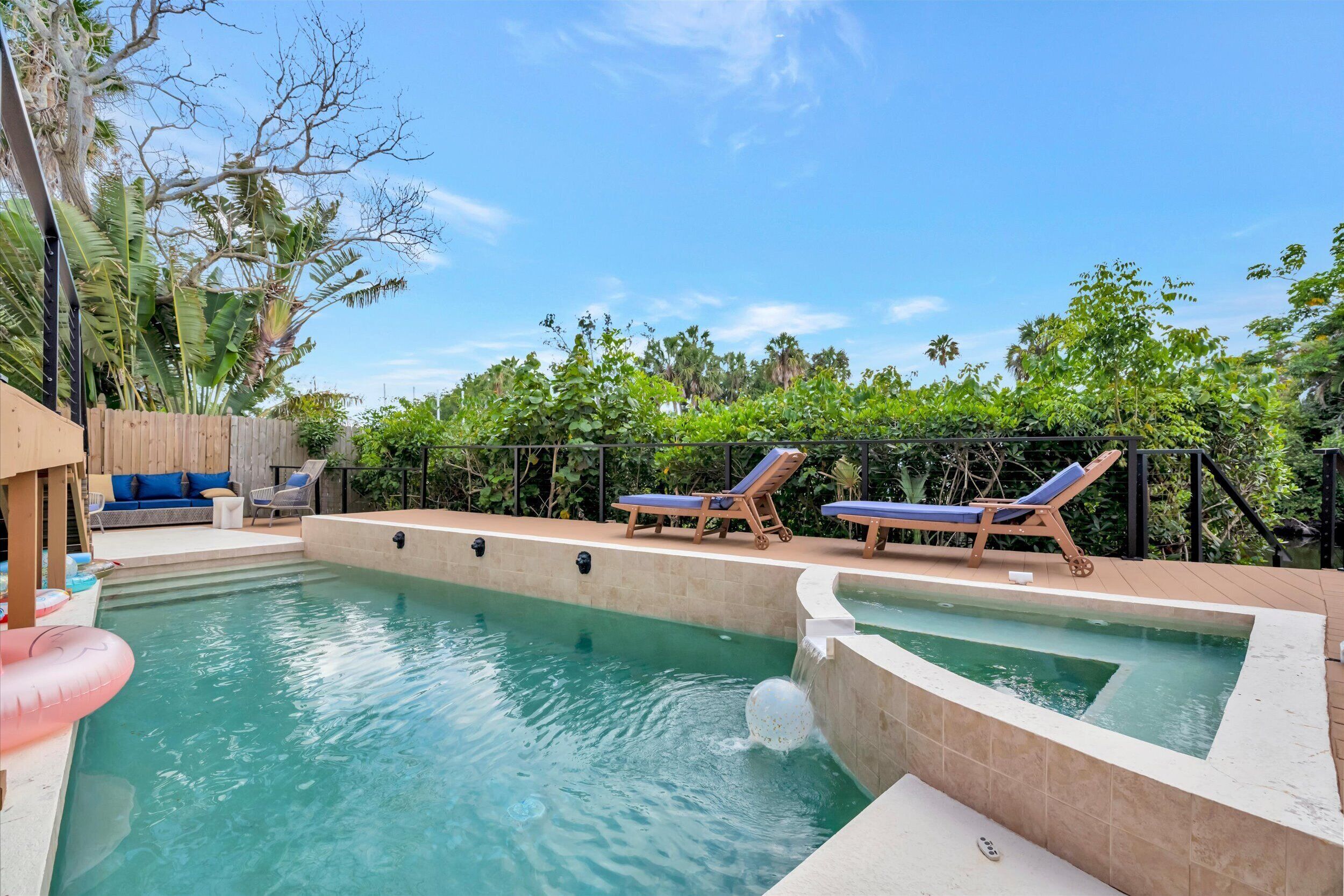 A swimming pool with two lounge chairs, a wooden deck, and a wooden fence.