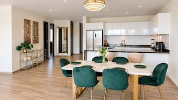 Una cocina moderna con armarios blancos, un refrigerador de acero inoxidable y una zona de comedor con una mesa blanca y sillas verdes.