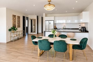 Une cuisine moderne avec des meubles blancs, un réfrigérateur en acier inoxydable et un coin repas comprenant une table blanche et des chaises vertes.