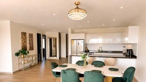 Une cuisine moderne avec des meubles blancs, un îlot central et un coin repas comprenant une table ronde et des chaises vertes.