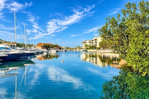 A marina with boats docked, calm water, and buildings in the background. - 3BR · Marina-view terrace · Pool (Puerto Aventuras)