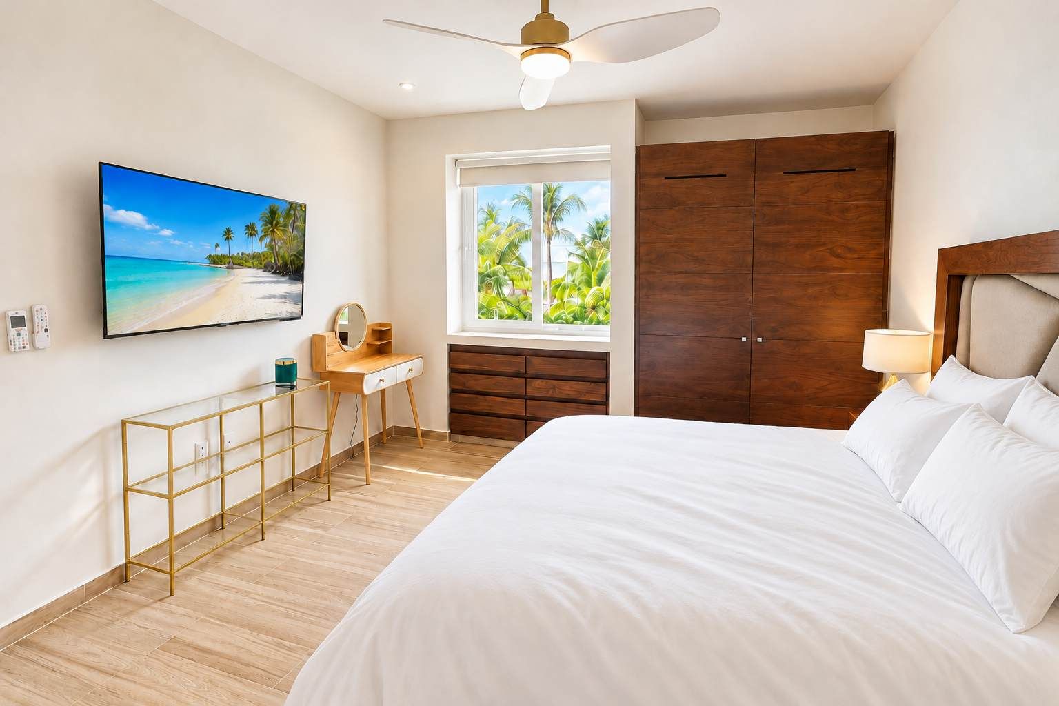 Ein Schlafzimmer mit Bett, Schminktisch mit Spiegel, Wandtelevison, Kleiderschrank und einem Fenster mit Blick auf Palmen.