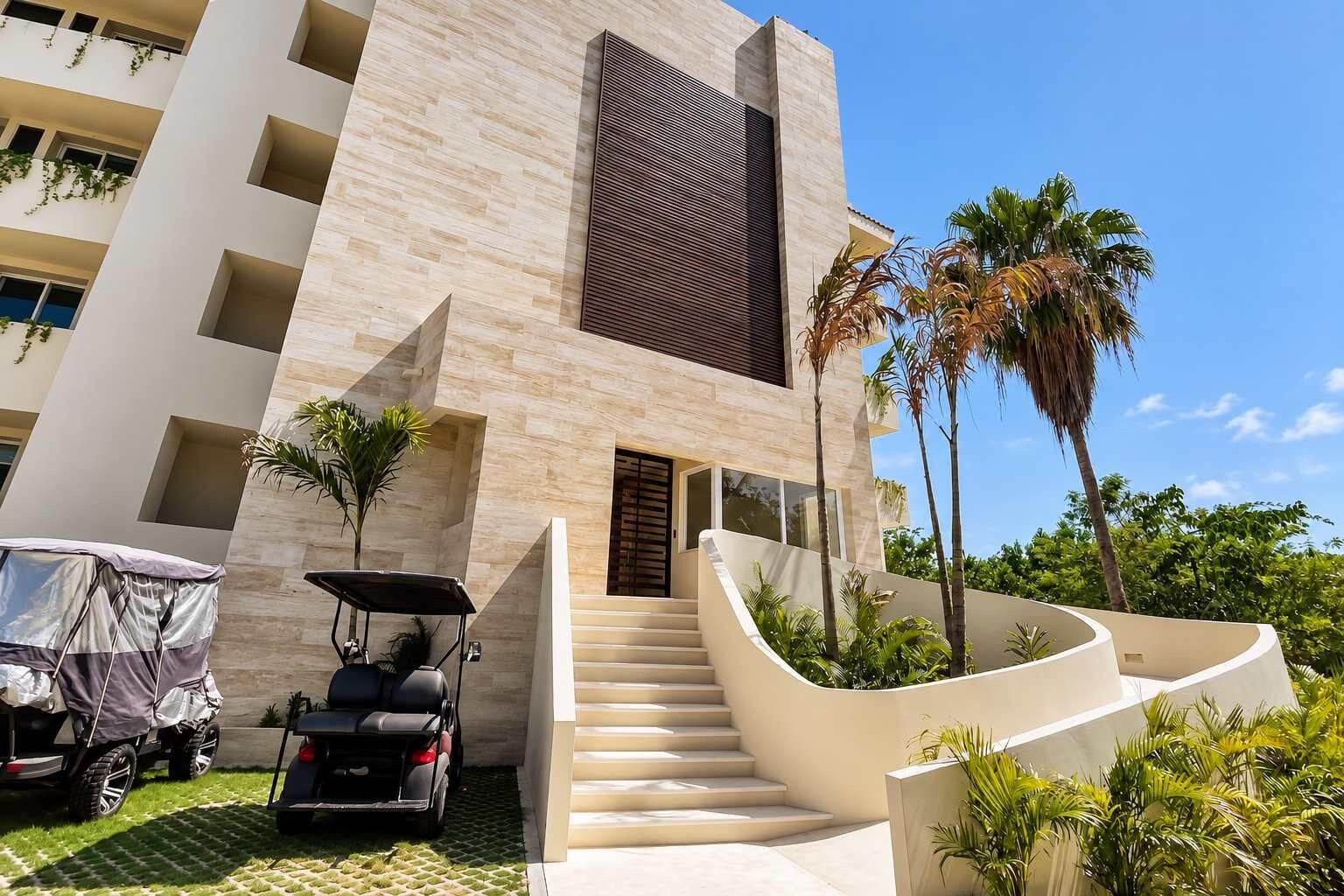 Un edificio moderno con una escalera que lleva a la entrada, rodeado de palmeras y follaje.
