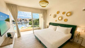 Une chambre d’hôtel avec un lit, une télévision, un balcon donnant sur la mer et un luminaire au plafond.