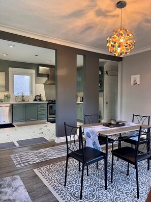 A modern dining area with a table set for four, a chandelier, and a view into the kitchen. - Spacious house near White Water Walk and many attractions (Niagara Falls)