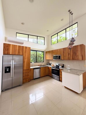 A modern kitchen with wooden cabinets, stainless steel appliances, and large windows. - Exclusive Villa with Pool in Bahía Ballena (Osa)