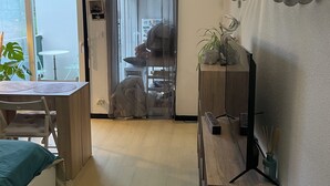 Una stanza con un tavolo da pranzo, sedie, un letto, un piccolo tavolino con una pianta, una sveglia a muro e una porta che dà su un'altra stanza.