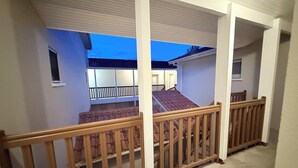 Un balcone coperto con ringhiere in legno, vista sullo stabile adiacente e cielo sereno.