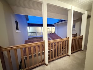 Un balcon extĂ©rieur abritĂ©, dotĂ© de balustrades en bois, offrant une vue sur lâimmeuble voisin et sâouvrant sur un ciel dĂ©gagĂ©.
