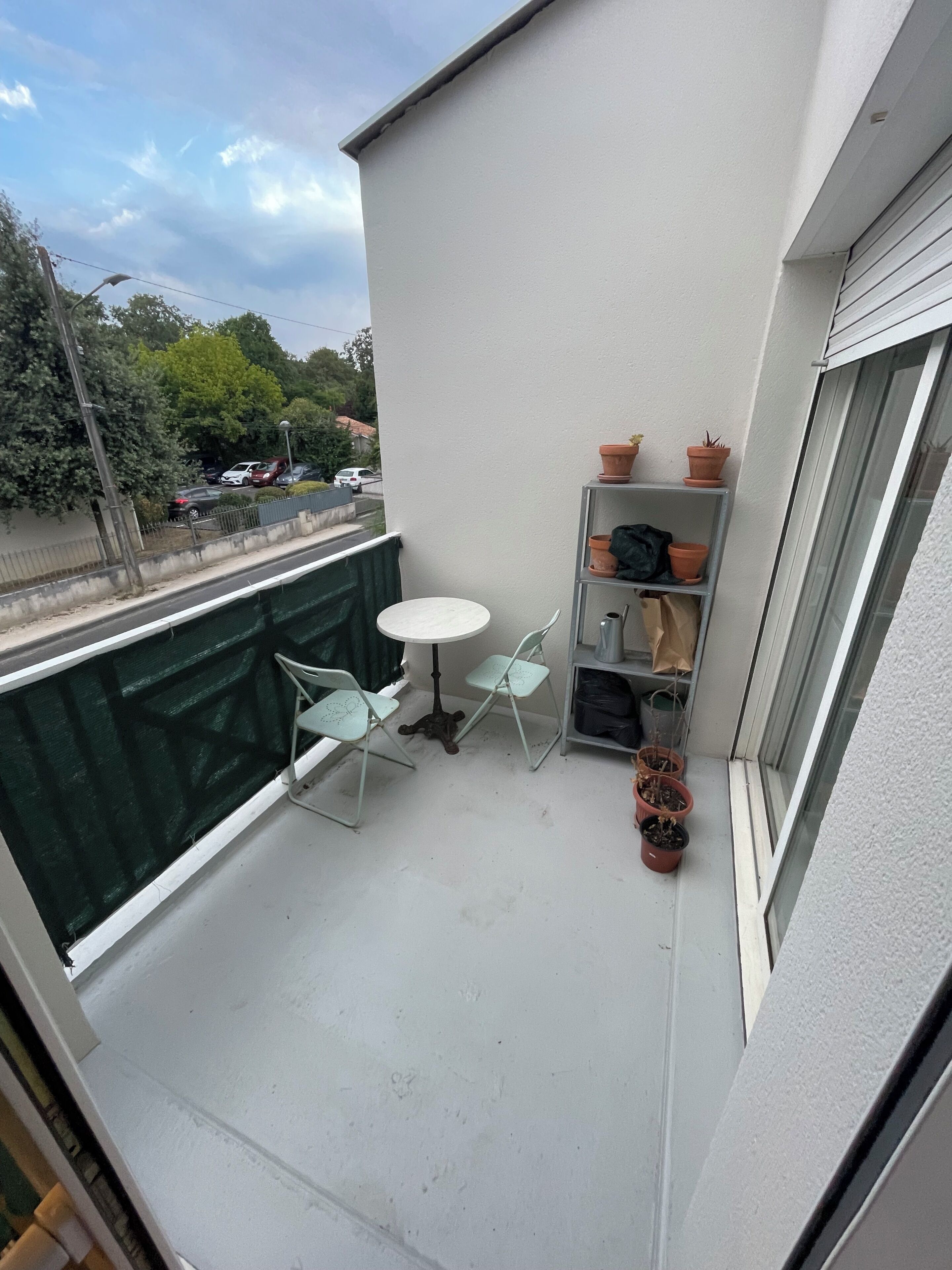 Un balcon avec une table et des chaises, une petite étagère avec des plantes en pot et une vue sur la rue.
