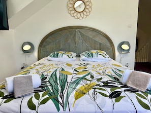 Ein Bett mit Bettdecke mit Blättermuster, zwei Nachttischlampen und ein runder Spiegel an der Wand.