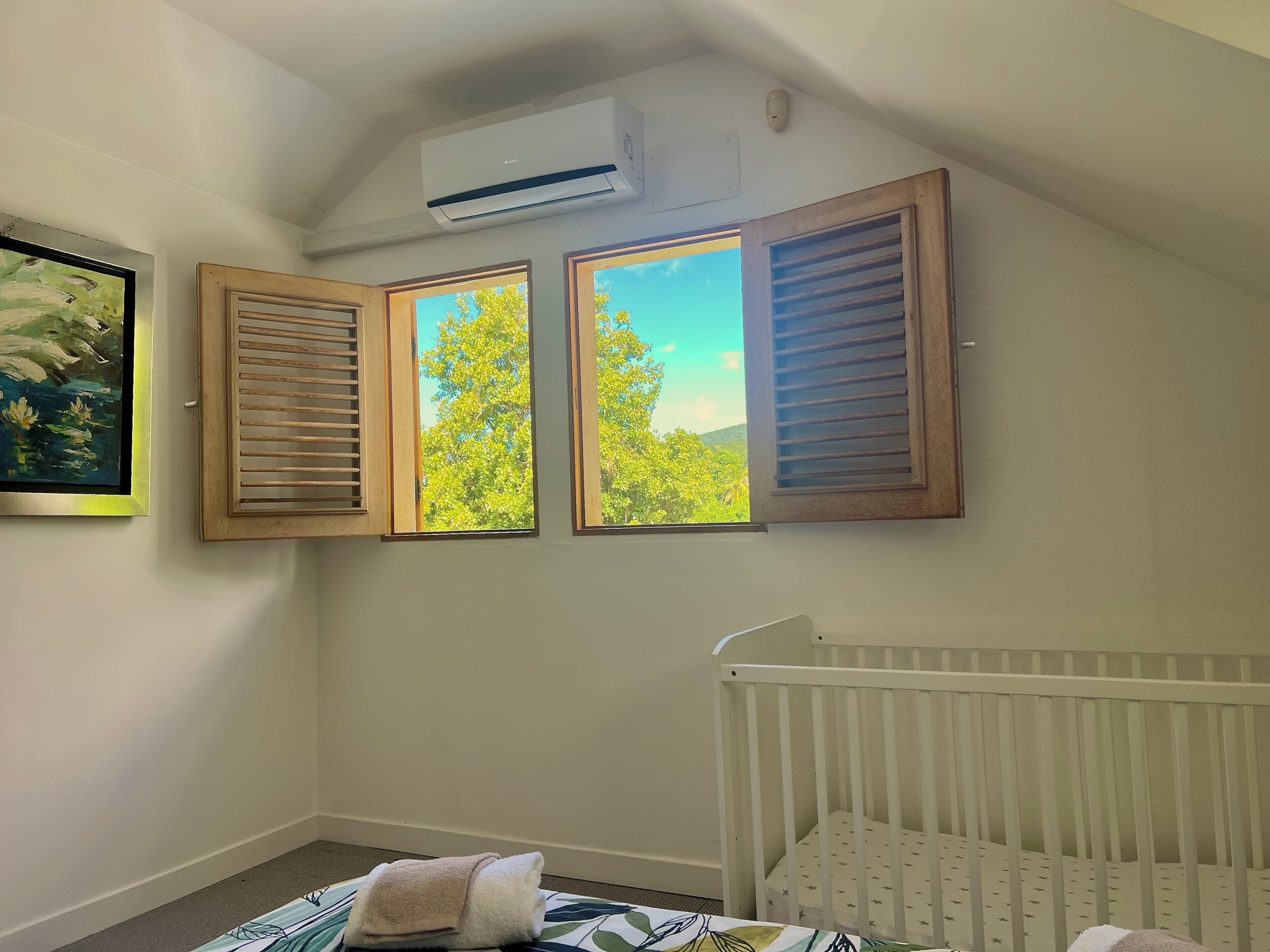A room with a crib, a painting on the wall, and three windows with wooden shutters.
