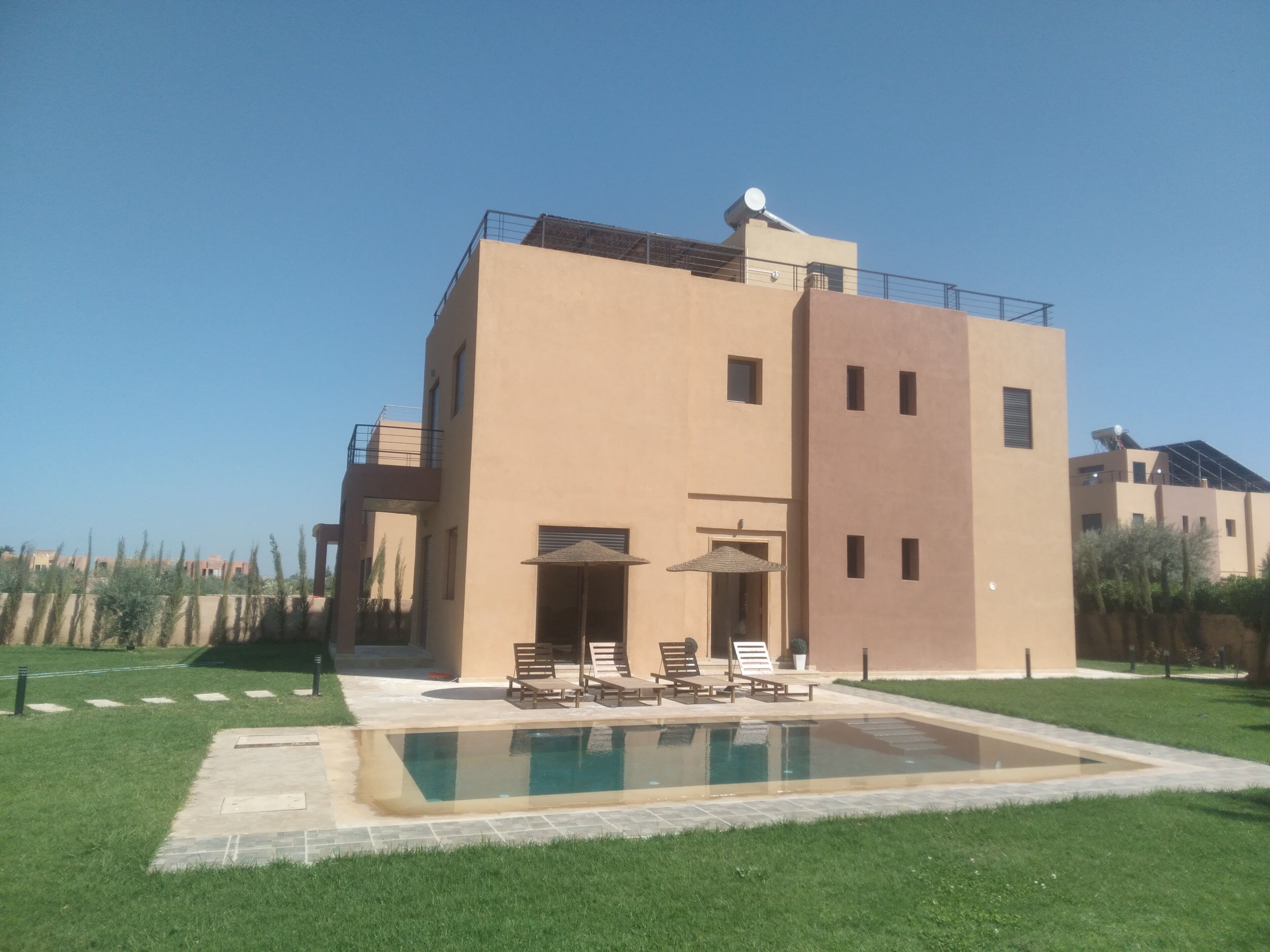 A modern building with a swimming pool, outdoor seating, and a clear sky.