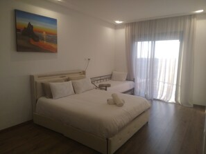 Ein Schlafzimmer mit einem großen Bett, einem kleineren Bett, einem Bild an der Wand und einem Fenster mit Vorhängen.