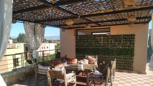 A terrace with a checkered floor, a table with chairs, a patterned ottoman, and a wall with green foliage. - Exceptional villa with private pool and 1300m² grounds (Marrakech)