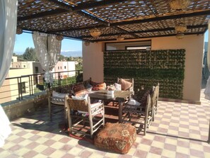 Eine Terrasse mit Schachbrettboden, einem Tisch mit Stühlen, einem gemusterten Hocker und einer Wand, die mit Grünpflanzen bewachsen ist.