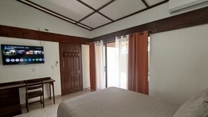 Un dormitorio con cama, escritorio, televisor montado en la pared y puerta corrediza que da a un balcón.