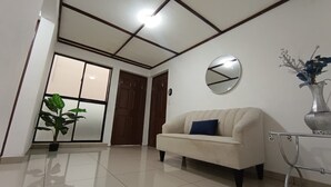 Una habitación con sofá, planta en maceta, espejo y un florero sobre una mesa.