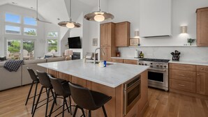 A modern kitchen with a large island, wooden cabinets, stainless steel appliances, and pendant lighting.