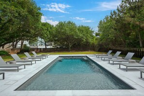 A rectangular swimming pool with a clear blue water surface, surrounded by white lounge chairs and a wooden fence. - New remodel 2026 - walk to beach, heated pool, hot tub, dogs ok (Nags Head)