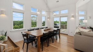 A spacious dining area with a wooden table and chairs, large windows with a view of greenery, and a modern ceiling light fixture.