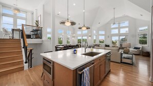 A spacious kitchen with a large island, wooden staircase, and ample natural light from large windows.