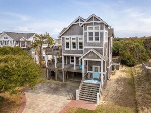 A multi-story beachfront house with a balcony, a small porch, and a staircase leading to the entrance. - New remodel 2026 - walk to beach, heated pool, hot tub, dogs ok (Nags Head)