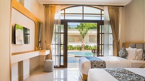 A hotel room with a bed, a TV, a small trash bin, and a view of a pool and greenery. - Sandat Mas Uluwatu (Uluwatu)