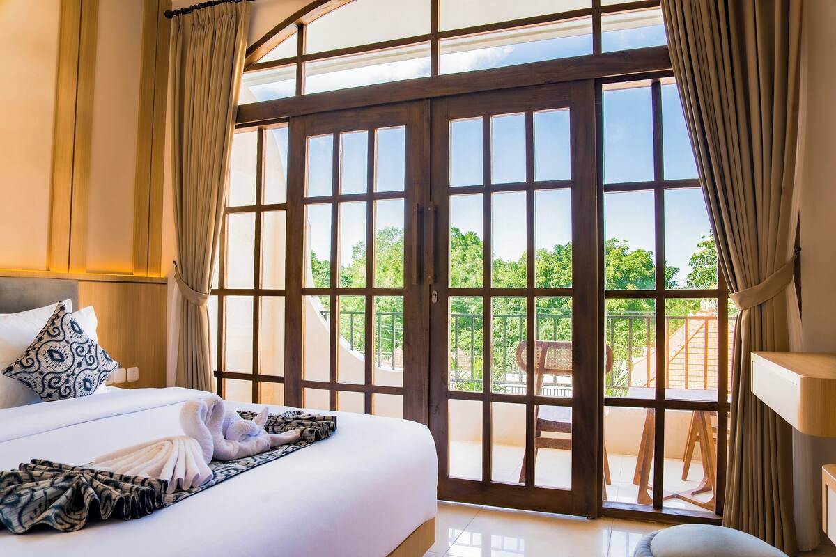 Habitación de hotel con un ventanal grande, una cama con toallas ordenadas y vistas al exterior.