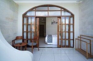 Quarto com cama, uma cadeira, uma mesa pequena e um banco de madeira.