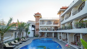 A hotel courtyard with a swimming pool, lounge chairs, and a multi-story building with balconies.