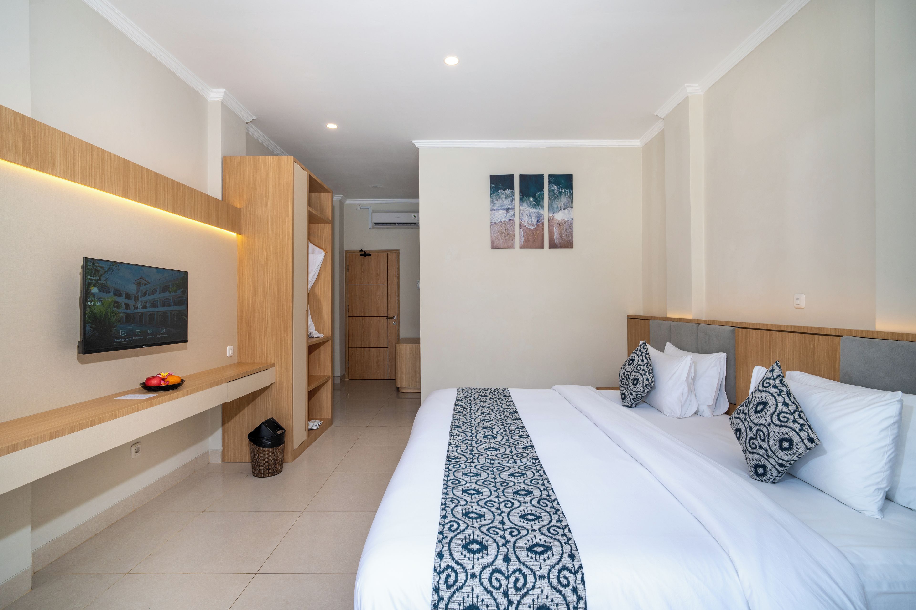 Quarto de hotel com cama, televisão, guarda-roupa e um pequeno cesto de lixo.