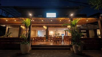 Un restaurante con zona de estar exterior cubierta, suelo de madera y plantas en macetas.