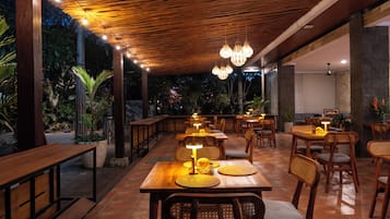 An outdoor dining area with wooden tables and chairs, string lights, and potted plants.