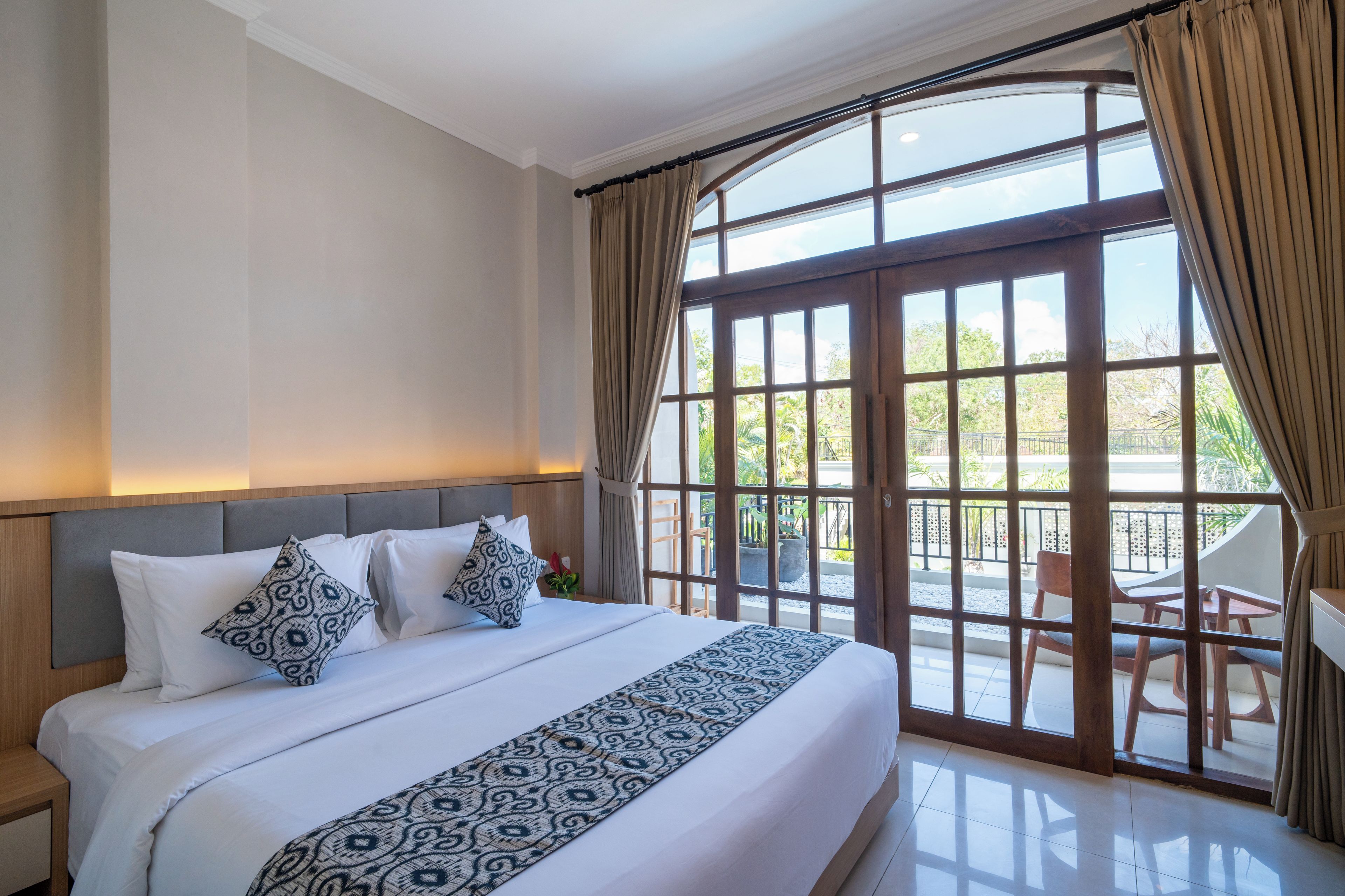 Une chambre d’hôtel avec un grand lit, une tête de lit et une vue sur l’extérieur grâce à une porte vitrée.