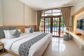 A hotel room with a large bed, a desk, a TV, and a view of a swimming pool. - Sandat Mas Uluwatu (Uluwatu)