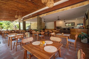 Um restaurante amplo, com mesas e cadeiras de madeira, grandes janelas e um espaço de bar.
