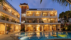 A multi-story hotel with a swimming pool, balconies, and a traditional architectural style.