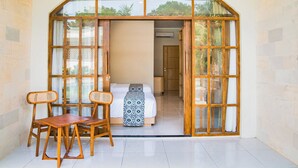 A room with a bed, a wooden table, two chairs, and a large arched window. - Sandat Mas Uluwatu (Uluwatu)