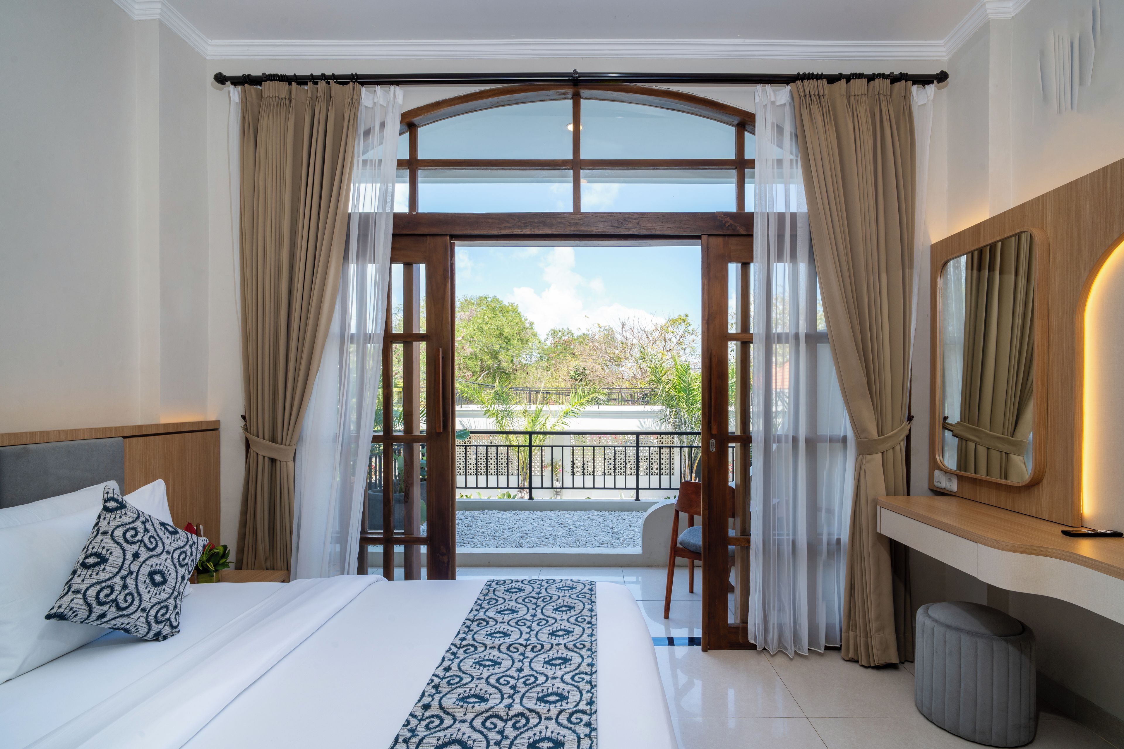 A hotel room with a large bed, a view of a balcony, and a wooden-framed window.