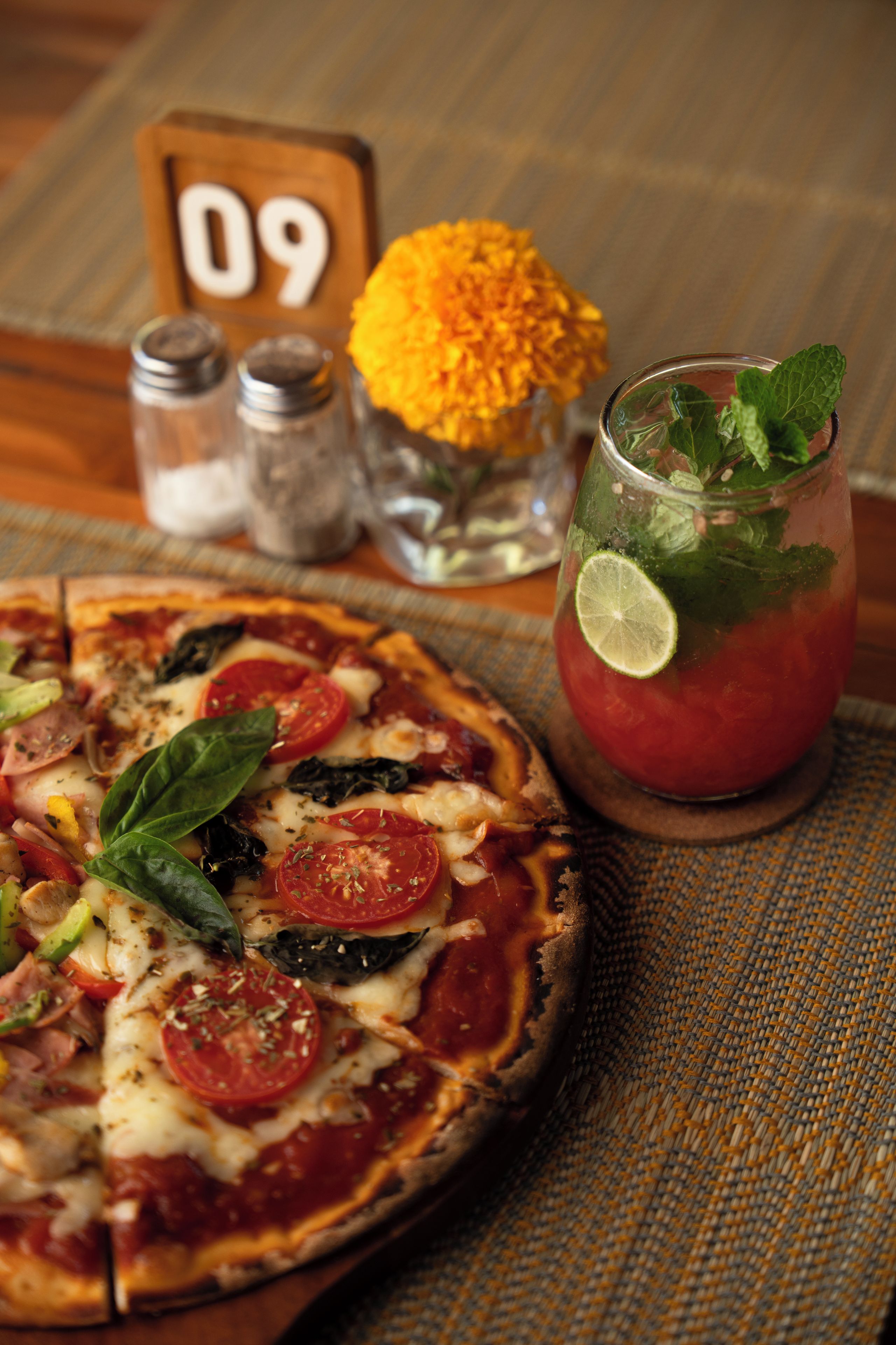 A pizza with various toppings and a glass of red beverage with a lime wedge.