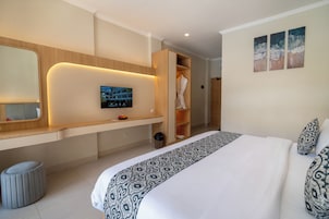 Una habitación de hotel moderna con una cama grande, un televisor montado en la pared, un tocador de madera y un vestidor.