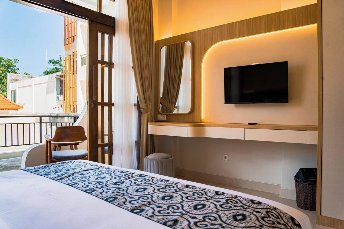 Habitación de hotel con cama, televisión montada en la pared, una mesita y una silla.