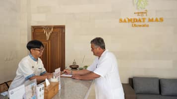A reception desk with a wooden counter, a guestbook, and a sign indicating the hotel name 'SANDAT MAS Uluwatu'.