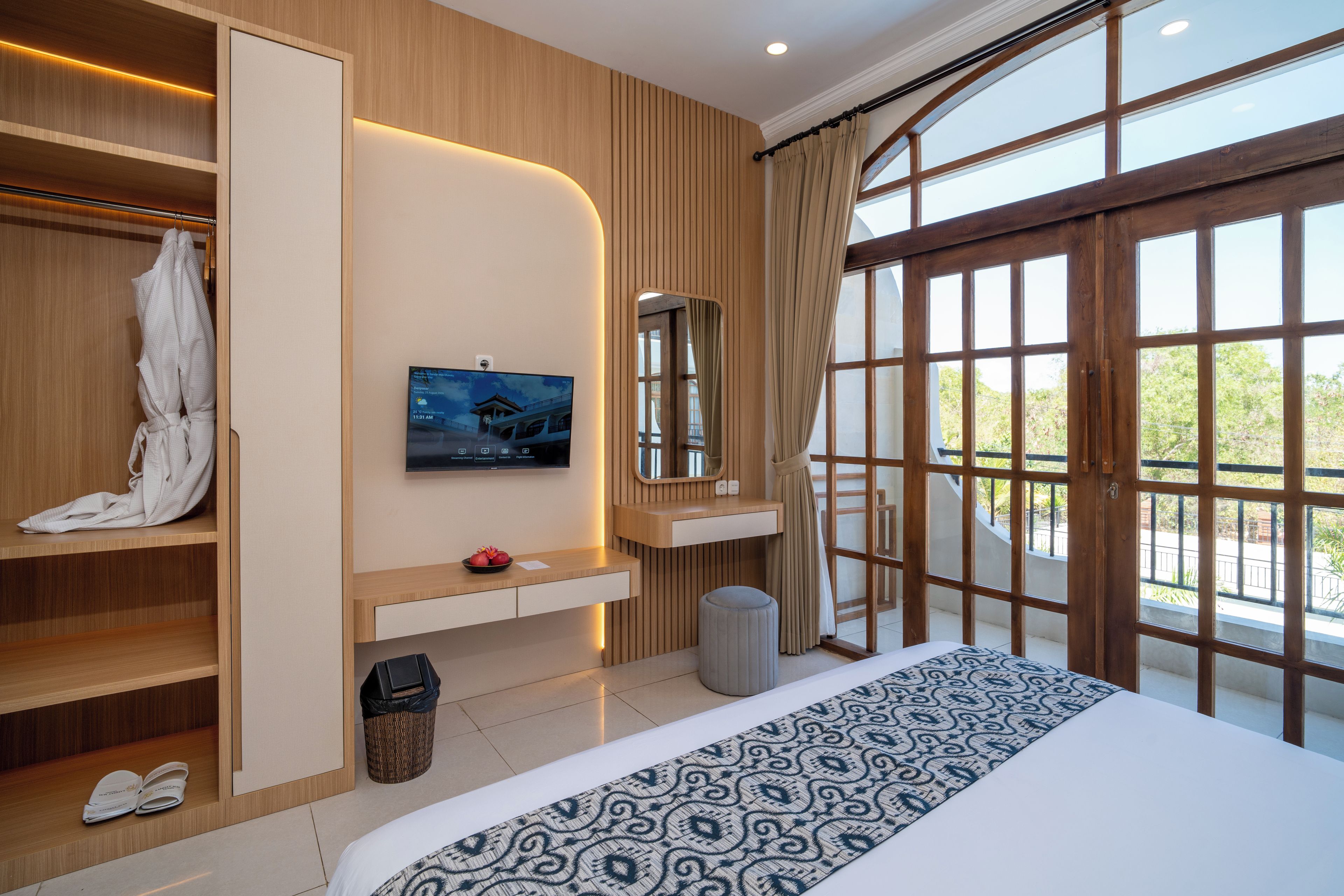 A hotel room with a large bed, a television, a wardrobe, and a window with a view of greenery.