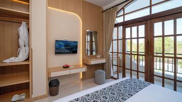 A hotel room with a large bed, a television, a wardrobe, and a window with a view of greenery.