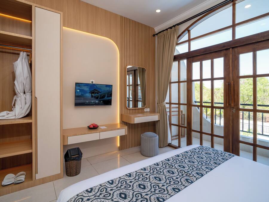 A hotel room with a large bed, a television, a wardrobe, and a window with a view of greenery.
